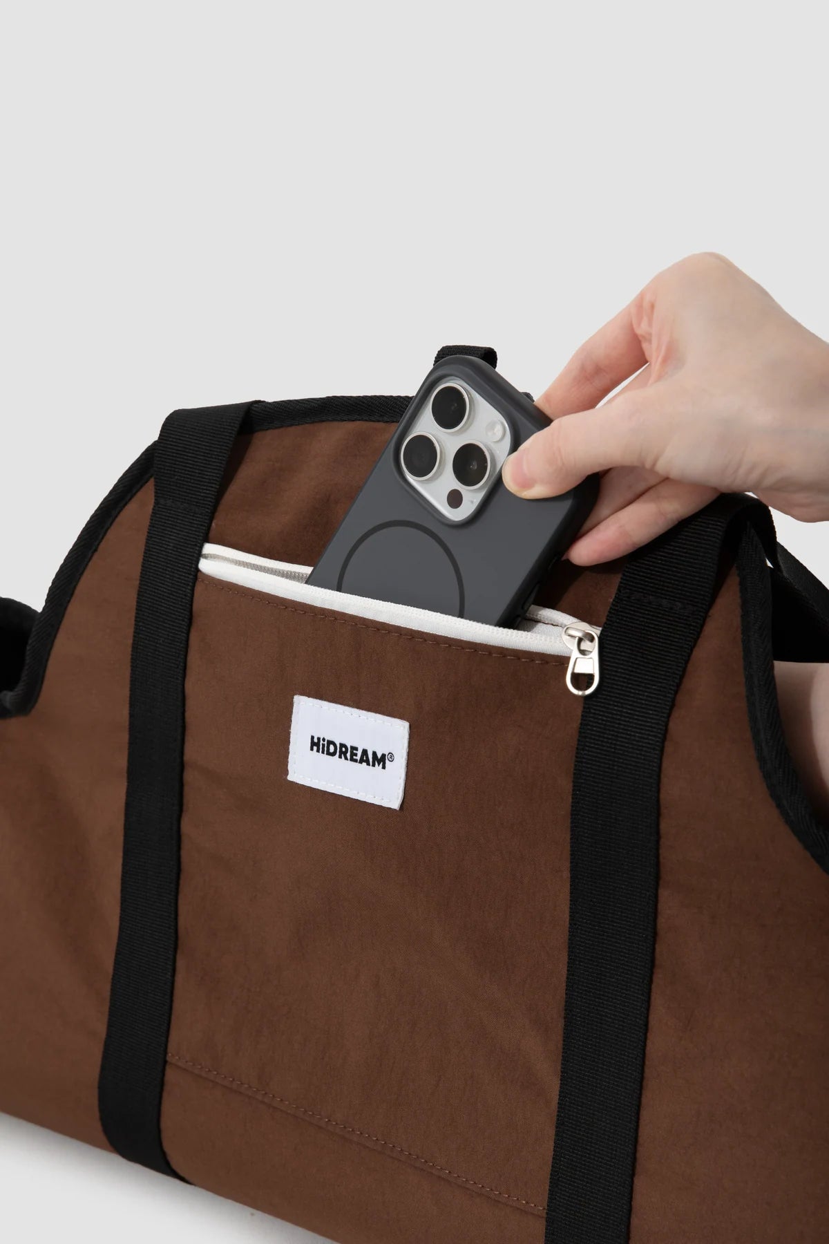 A hand placing a phone in the outer zip pocket of the brown Baguette carrier