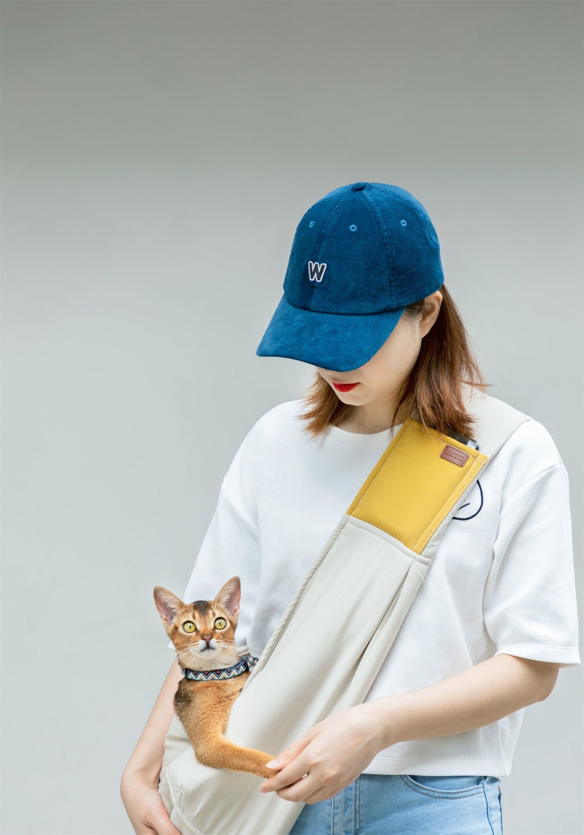 Cat held close in the cream and yellow cotton pet sling