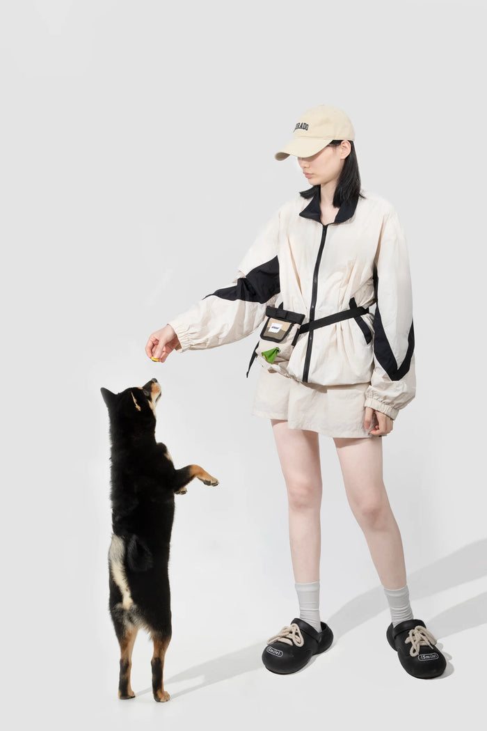 A person wearing the Beige treat pouch and offering a treat to a dog in the studio