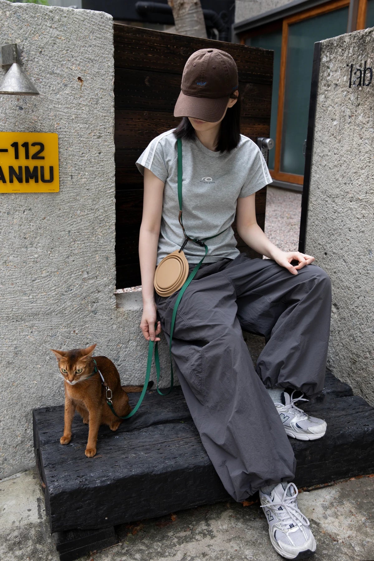 Owner sitting beside a cat wearing the yellow harness outdoors