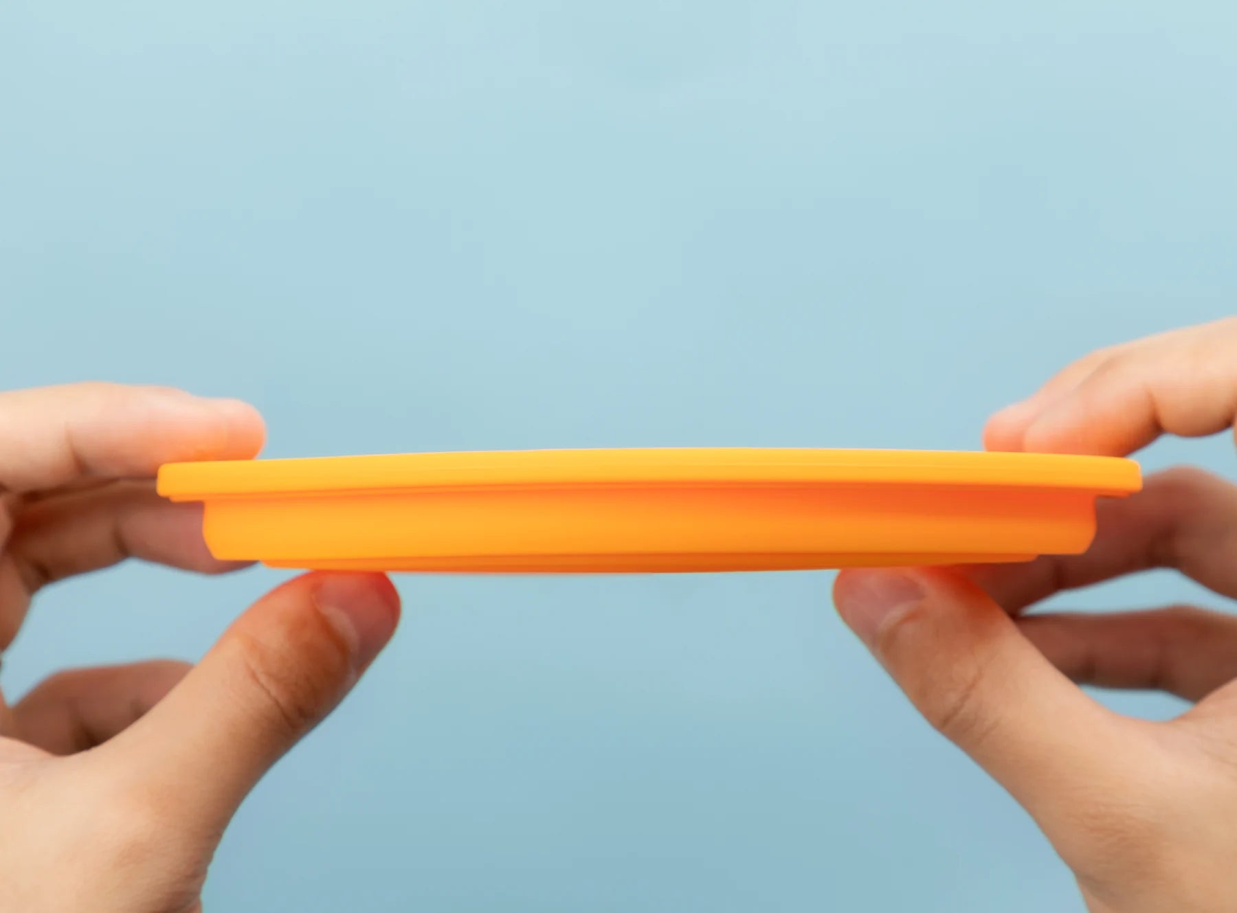 Hands pressing the orange silicone bowl flat